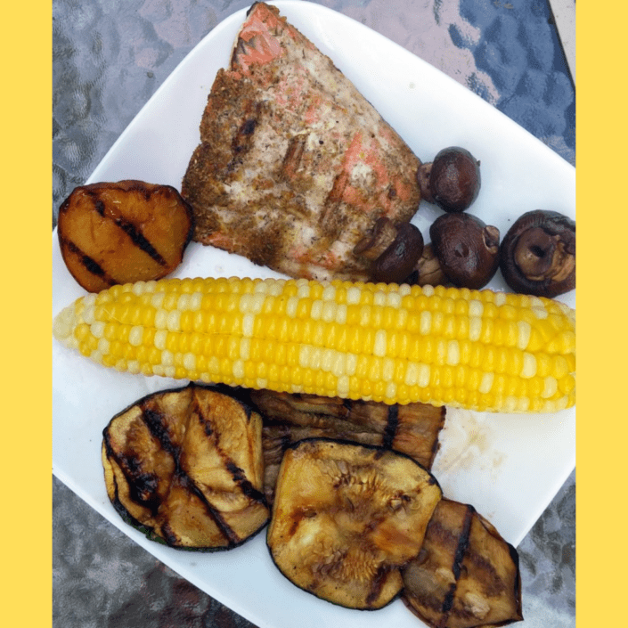 Deck dinner consisting of salmon, corn on the cob and roasted vegetables.
