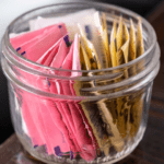 Packets of artificial sweeteners in a glass jar.