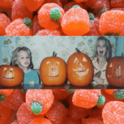 Two young girls sticking their tongues out with four jack-o-lanterns on the table.