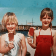 Two young girls at the beach holding ice creams.