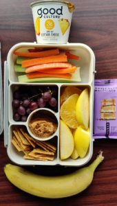 bento box full of veggies, fruits, cottage cheese, peanut butter, crackers, protein bar and banana