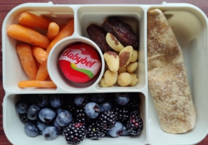 Bento box with tuna wrap, blueberries, blackberries, carrots, cheese, dates and nuts.