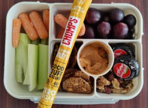 Bento box with meat stick, cheese, grapes, crackers, carrots, celery, nuts and peanut butter.