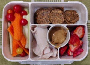 Bento box with turkey, crackers, peanut butter, strawberries, tomatoes, carrots and celery.